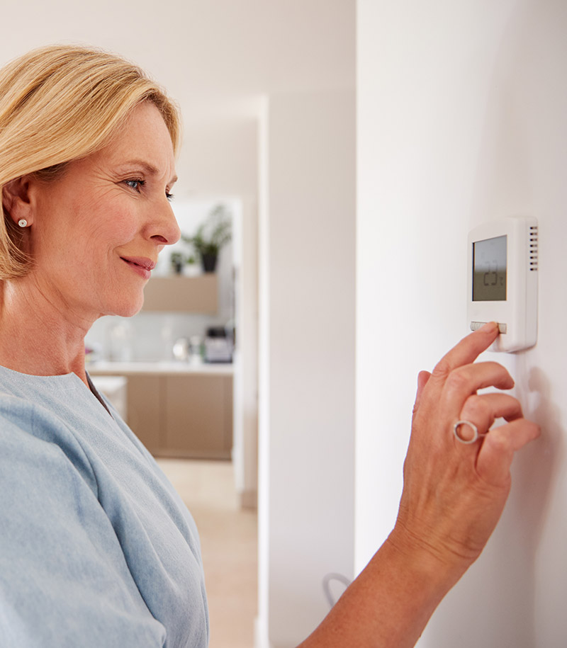 Woman adjusting a wall-mounted thermostat inside a bright, modern home.